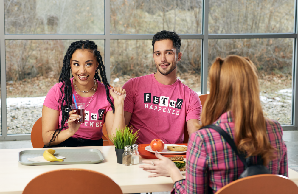 Two friends in Fetch Happened tees at a cafeteria table