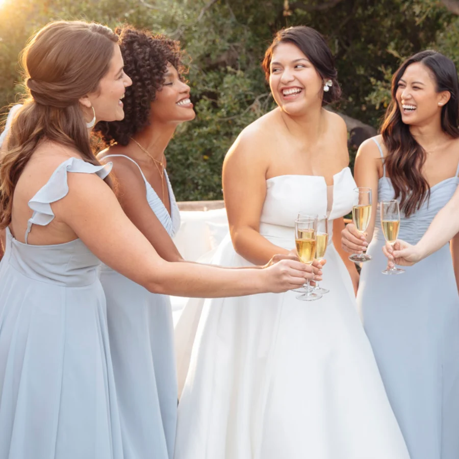 Bridesmaids in Poppy dresses laughing and toasting with the bride